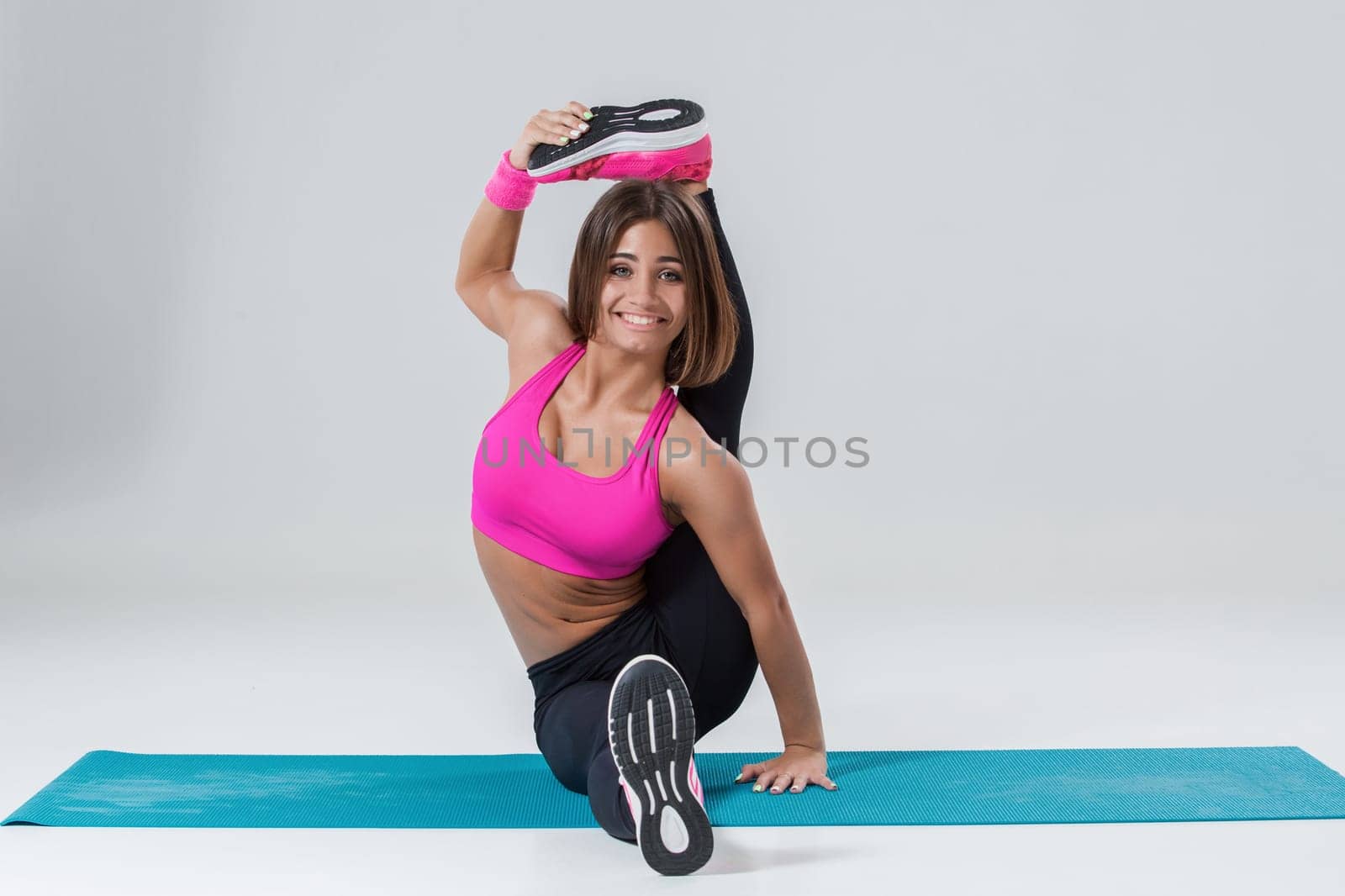 Sport and active lifestyle. Sporty flexible girl fitness woman in pink sportswear doing stretching exercise on light background.