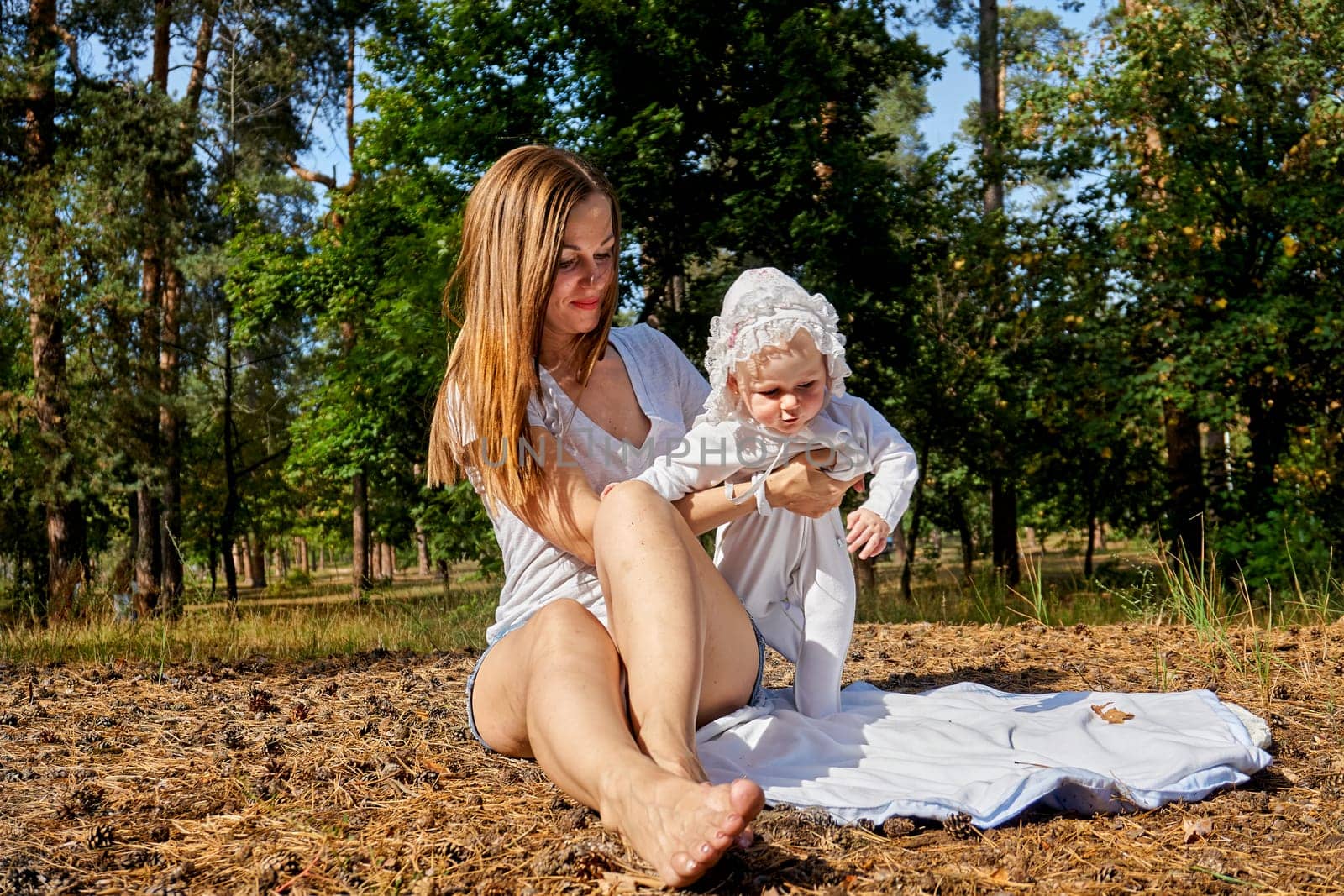 a very young child, especially one newly or recently born. Young pretty mother with a cute breast newborn baby in a sunny forest.