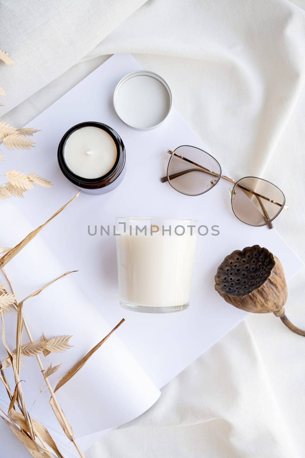 Soy wax aroma candles in brown jar on bed , with fashion glasses. Candle mockup design. Mockup soy wax candle in natural style.