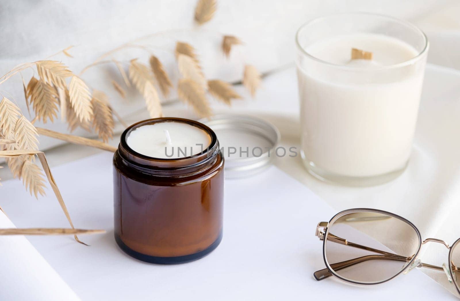 Soy wax aroma candle in brown jar on bed , with fashion glasses. Candle mockup design. Mockup soy wax candle in natural style.