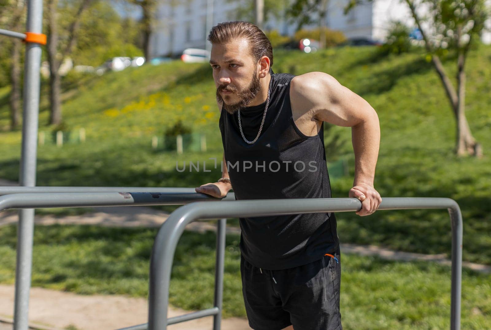 Athletic lebanese man in sportswear practicing dips on parallel bars, training triceps. Young middle eastern guy on playground. Sports health fitness routine, workout. Strength motivation. Outdoor gym