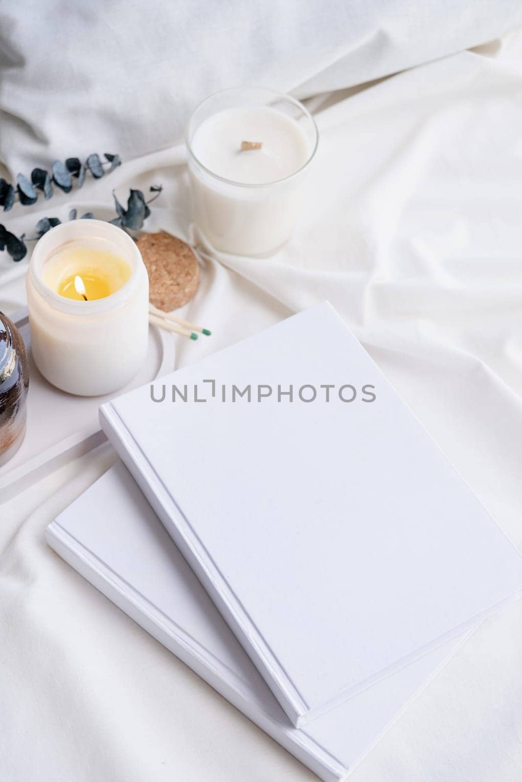 Soy wax aroma candle in white jar on bed with eucalyptus leaves. Candle mockup design. Mockup soy wax candle in natural style.