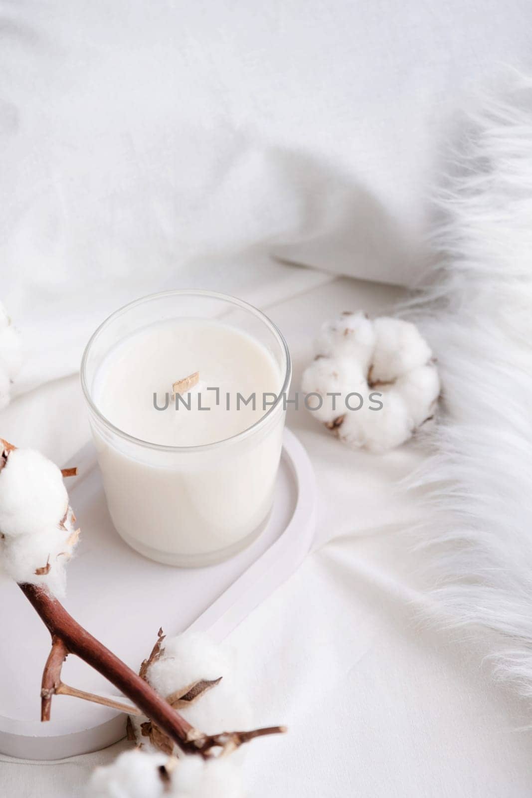 Soy wax aroma candle in white jar on bed with cotton branch. Candle mockup design. Mockup soy wax candle in natural style.