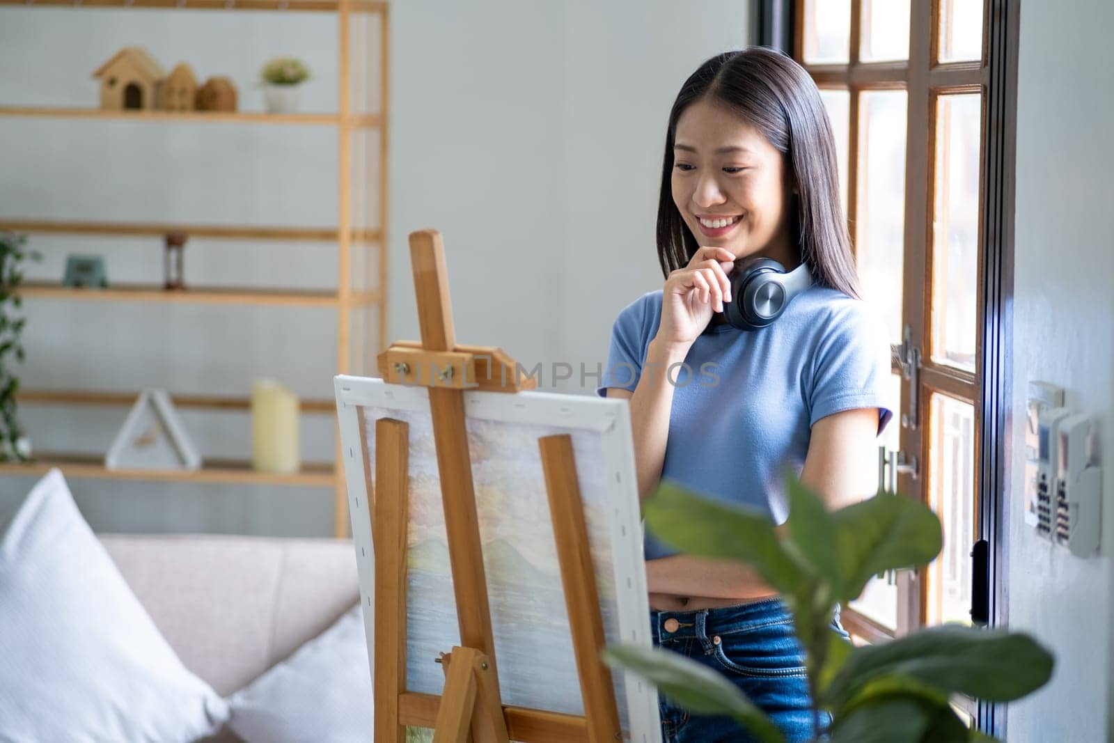 Young happy Asian woman chilling relaxing day off painting at home, female artist on canvas at home. hobby drawing. High quality photo