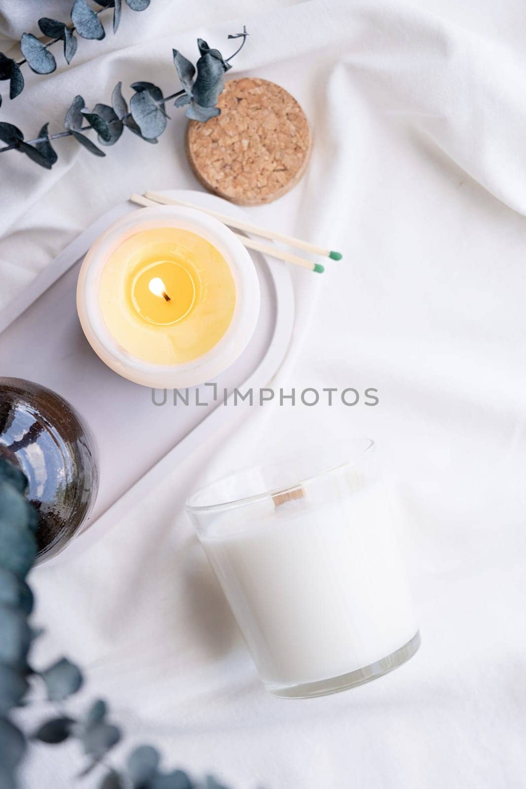 Soy wax aroma candle in white jar on bed with eucalyptus leaves. Candle mockup design. Mockup soy wax candle in natural style.
