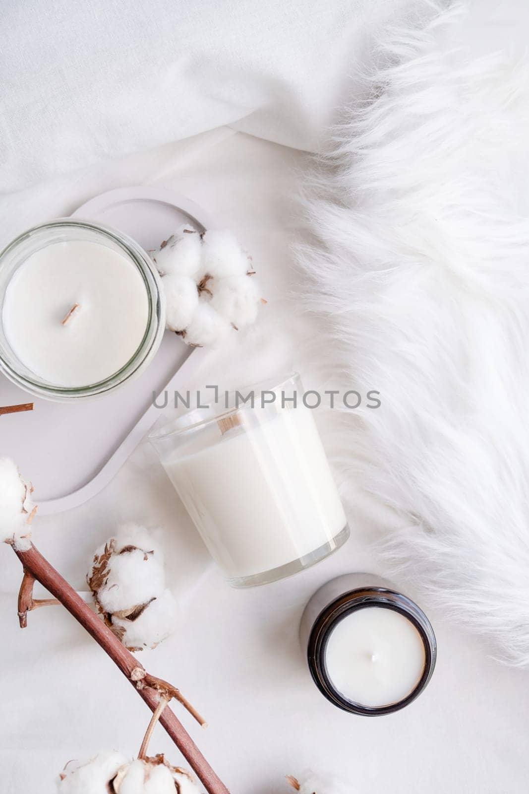 Soy wax aroma candle in white jar on bed with cotton branch. Candle mockup design. Mockup soy wax candle in natural style.