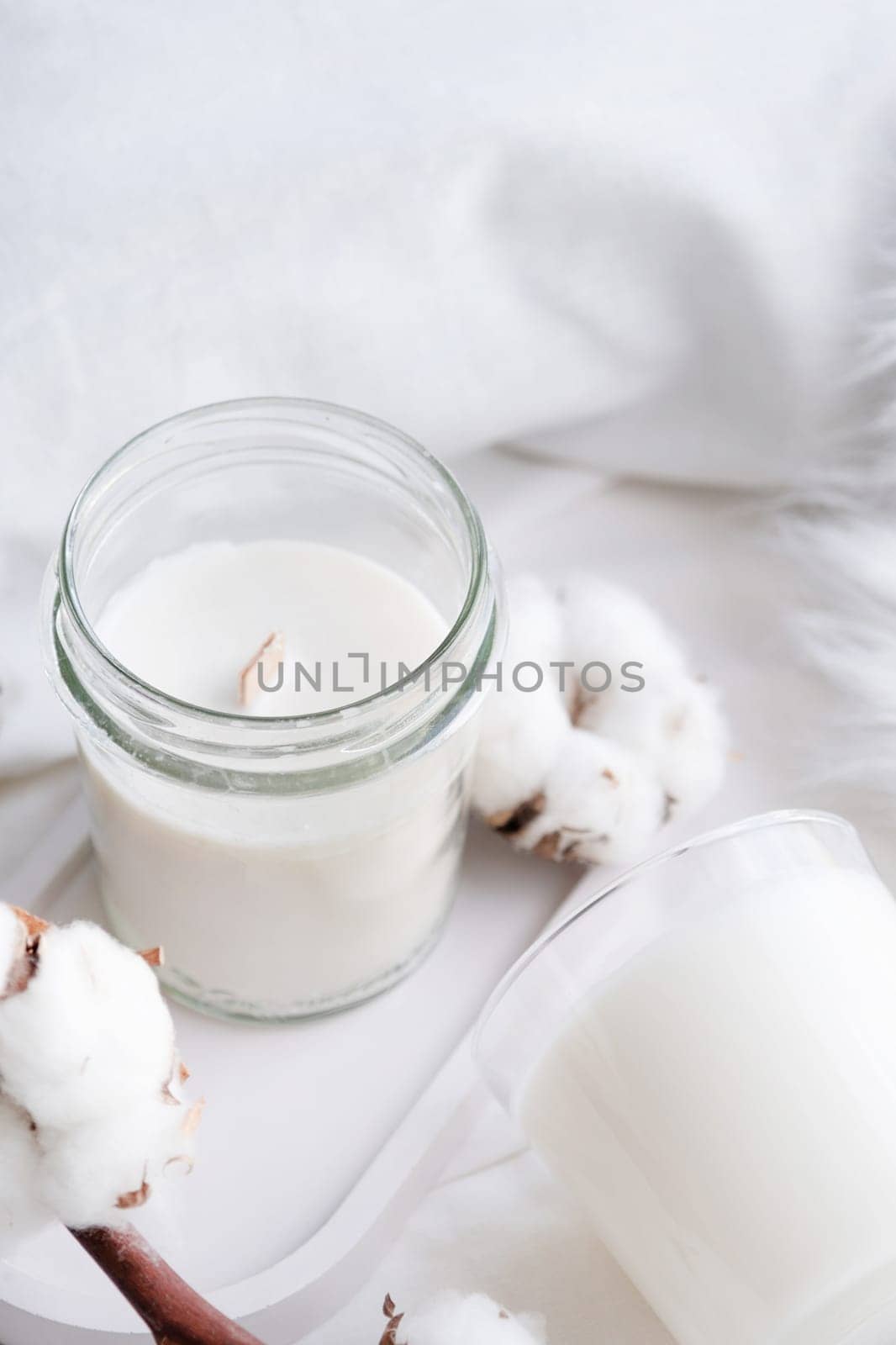 Soy wax aroma candle in white jar on bed with cotton branch. Candle mockup design. Mockup soy wax candle in natural style.