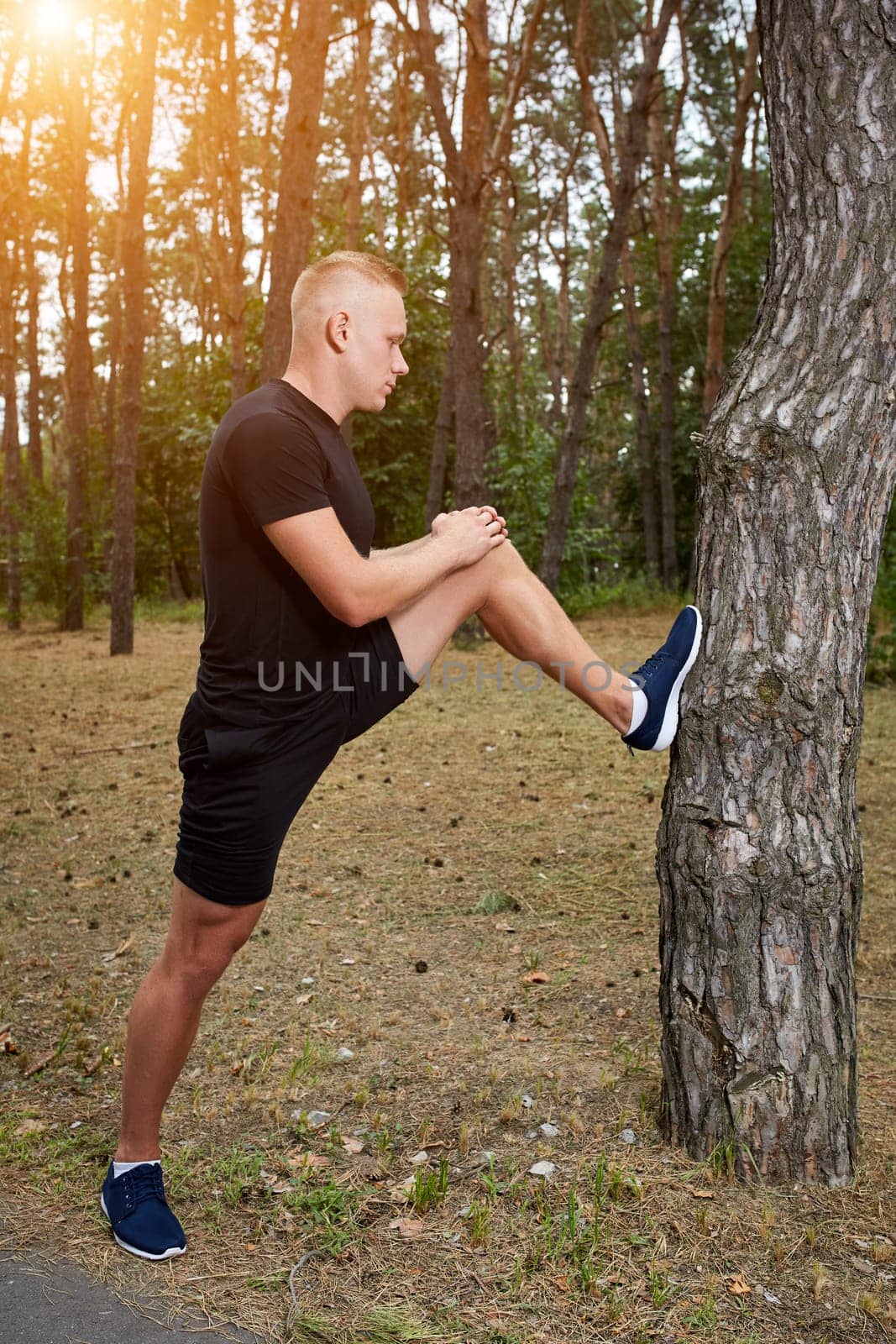 young athlete running in the forest, doing warm-up and stretching. with a sun flare