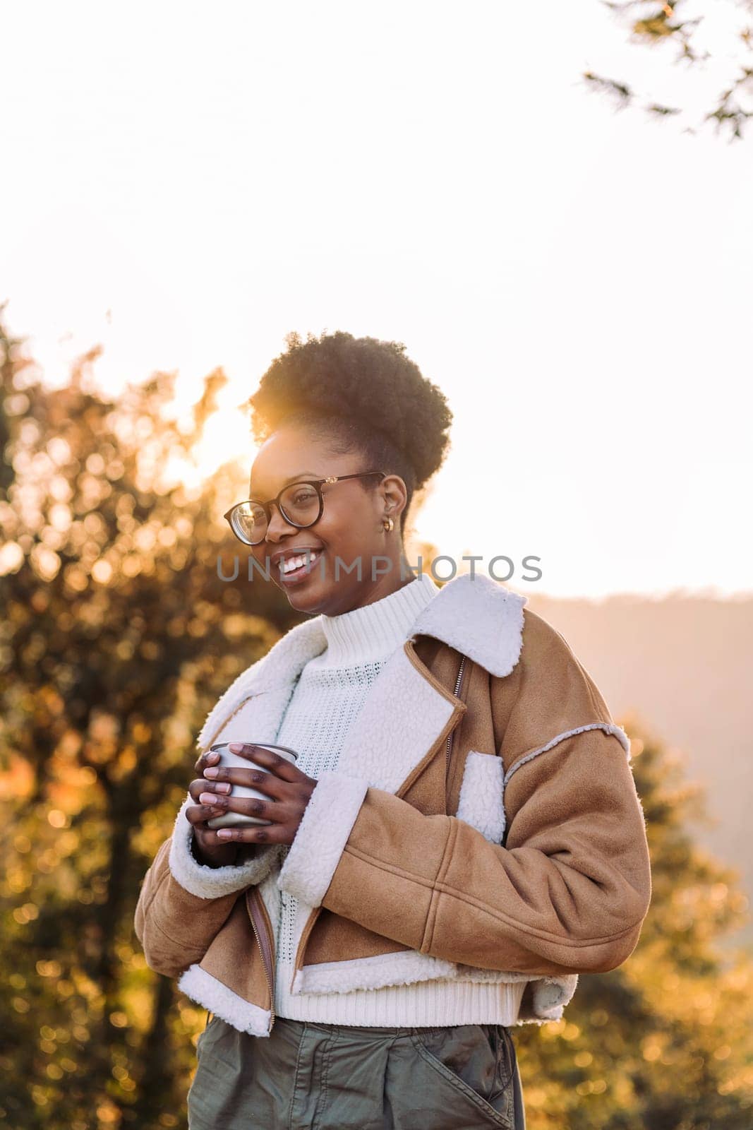 young african woman smiling happy in nature with a mug of hot drink in hand, concept of morning bliss and wilderness lifestyle, copy space for text