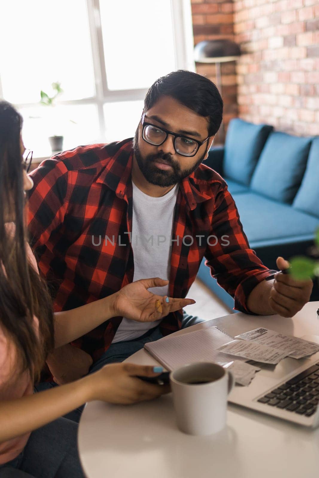 Young millennial indian husband and wife doing domestic paperwork, accounting job and reviewing paper bills, receipts at laptop computer, using online calculator and paying mortgage rent fees on internet - economic crisis