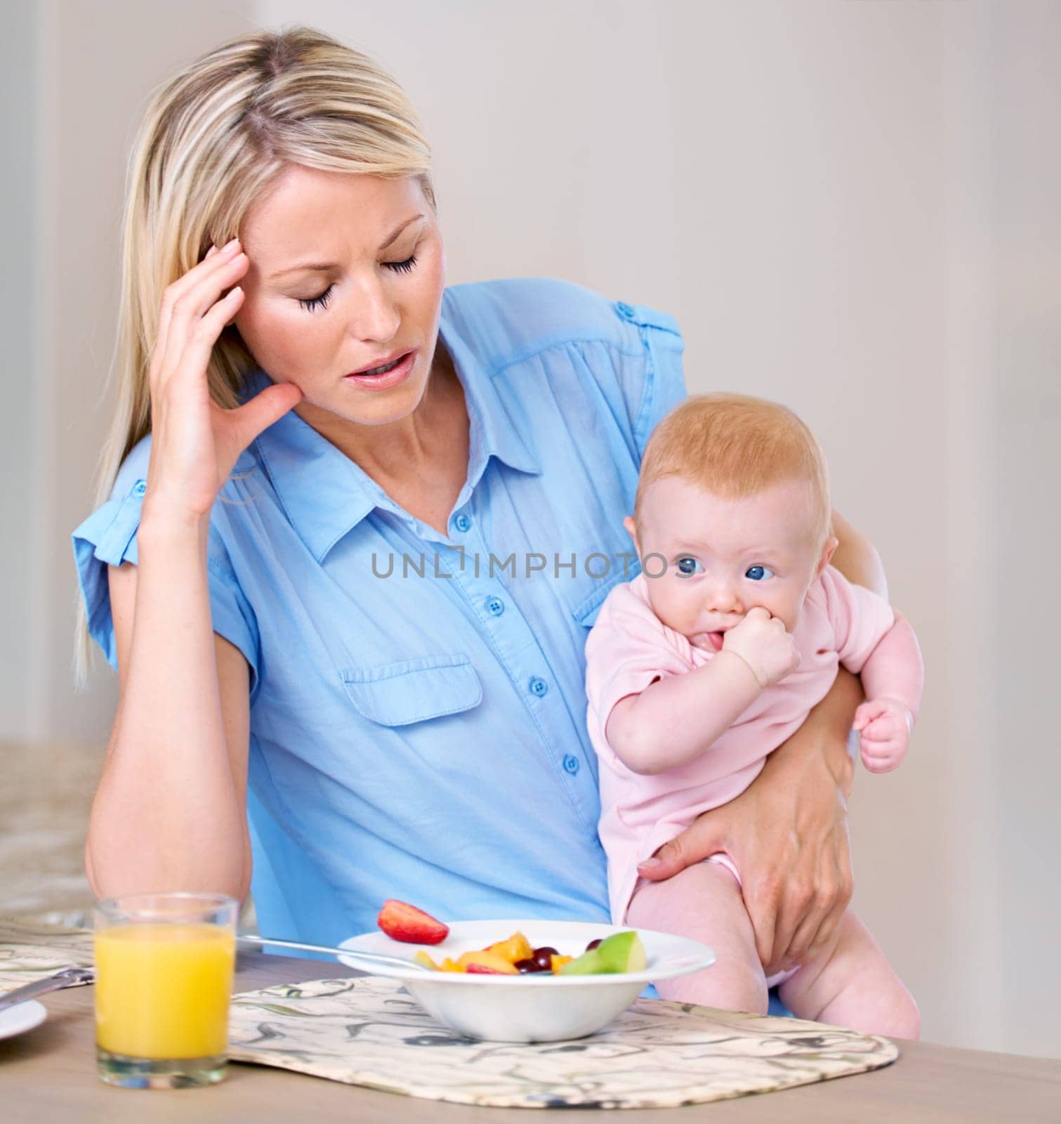 Motherhood blues. Young mother holding her baby at breakfast time looking tired