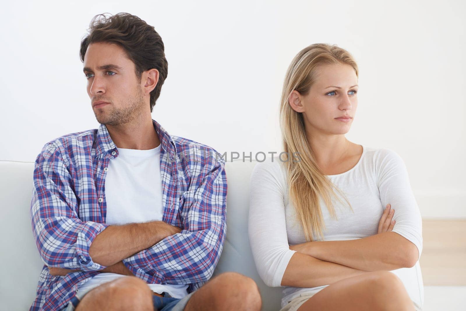 Communication breakdown. A disagreeing couple sitting with arms crossed and looking away from each other in upset