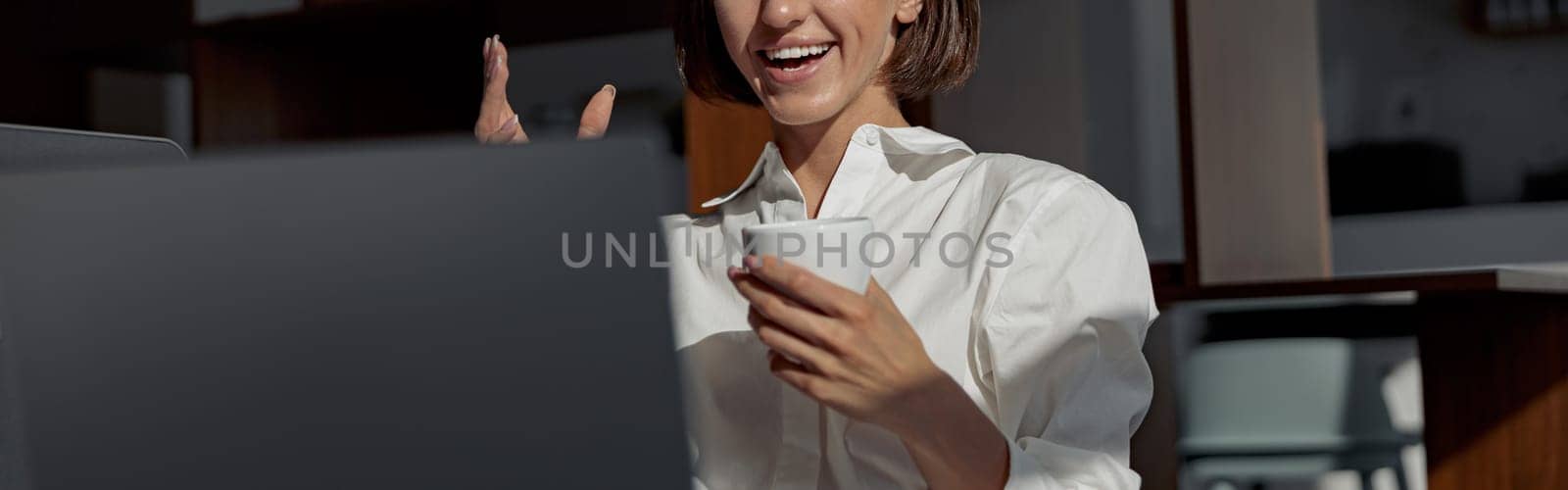 Businesswoman making video call to friends and showing sign V while working in modern office by Yaroslav_astakhov