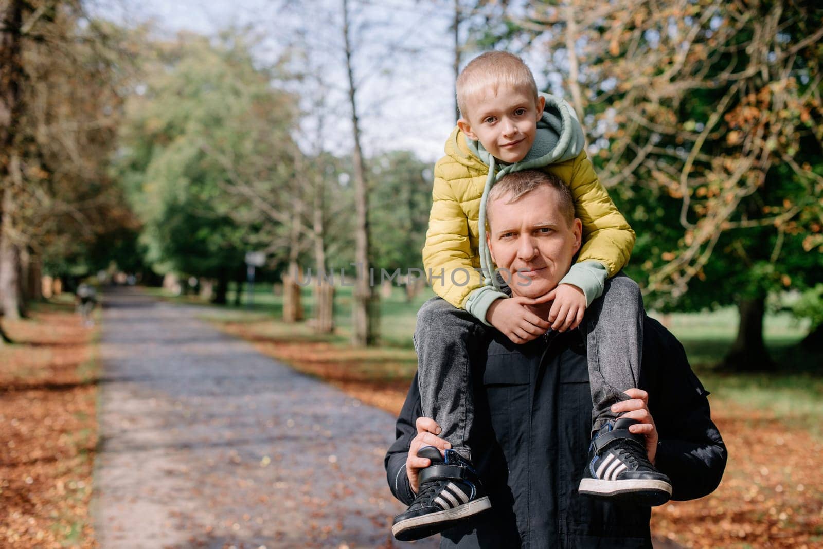 Dad holds on his son's shoulders. Beautiful family is spending time together outside. Dad and his little son are having fun on a roof terrace with view on a city. Sitting on father's shoulders and smiling.