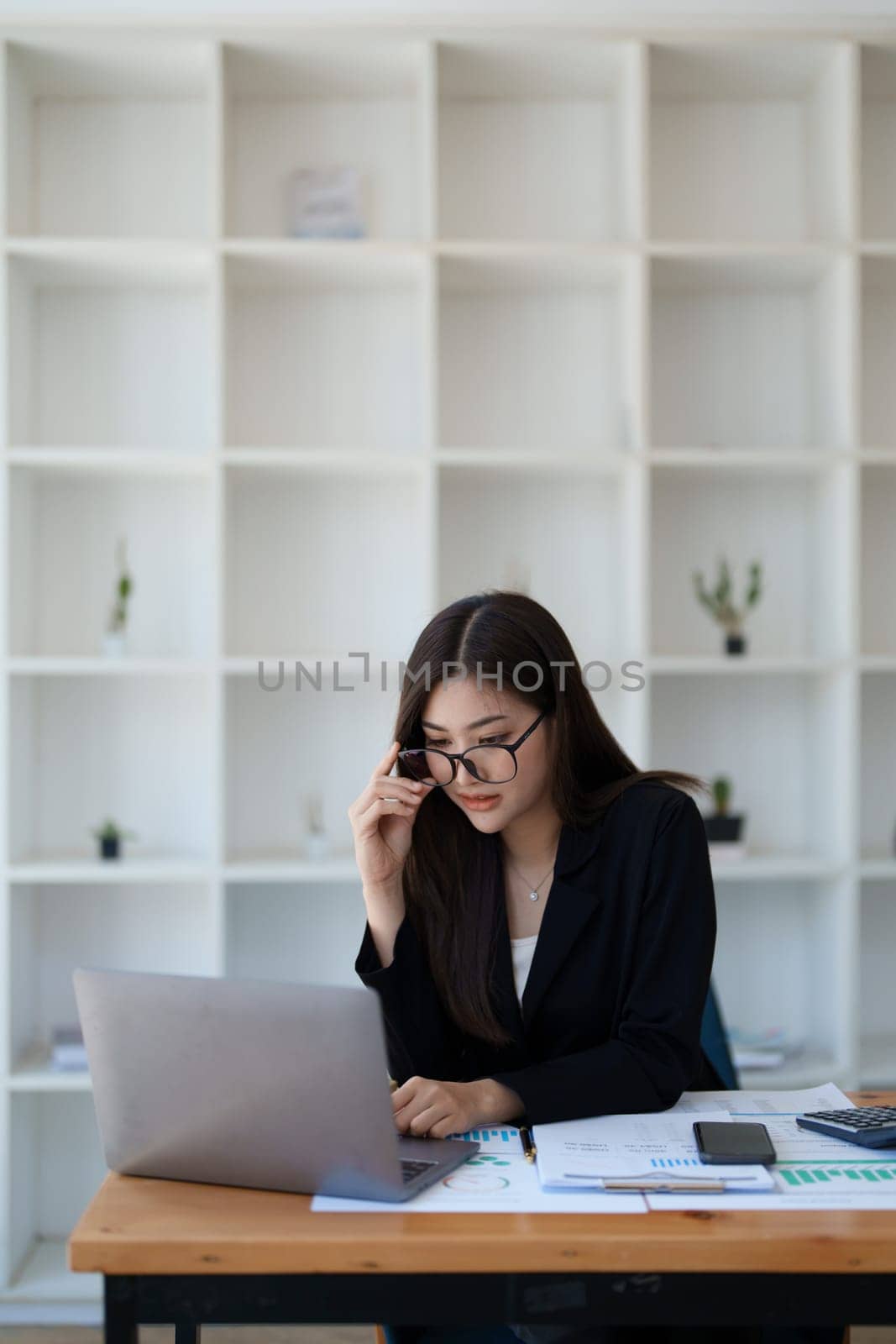 Portrait of a thoughtful Asian businesswoman looking at financial statements and making marketing plans using a computer on her desk.