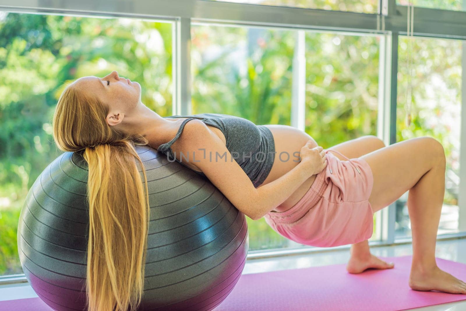 Pregnant woman exercising on fitball at home. Pregnant woman doing relax exercises with a fitness pilates ball. Against the background of the window.