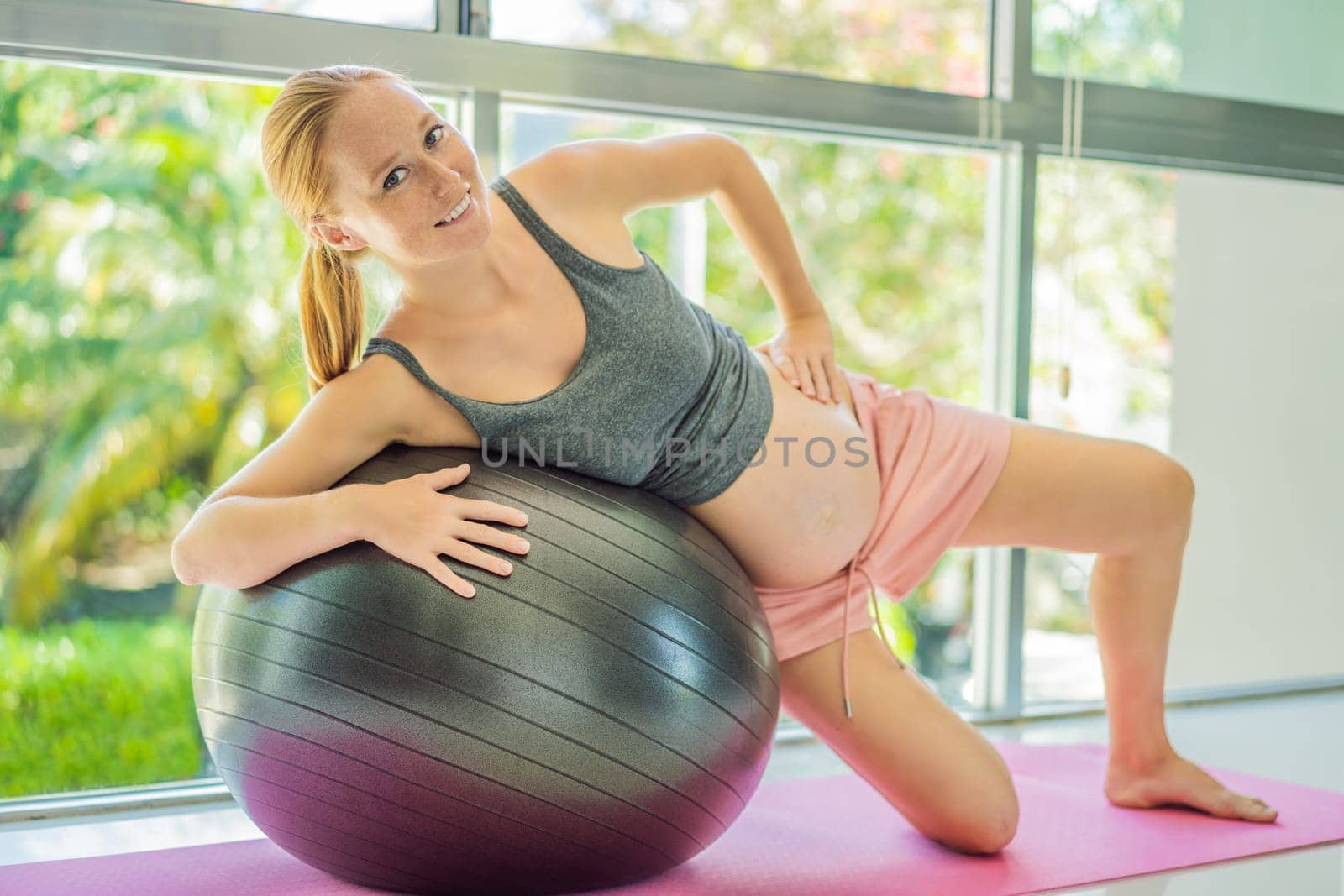 Pregnant woman exercising on fitball at home. Pregnant woman doing relax exercises with a fitness pilates ball. Against the background of the window.