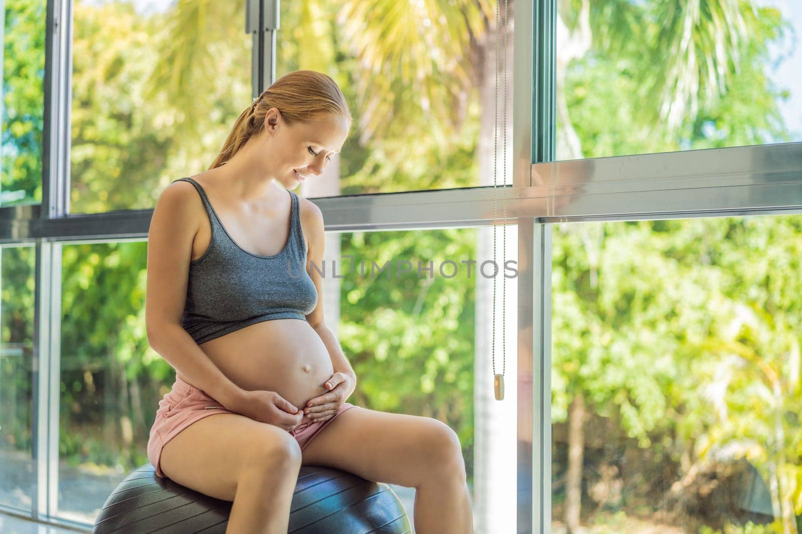 Pregnant woman exercising on fitball at home. Pregnant woman doing relax exercises with a fitness pilates ball. Against the background of the window.