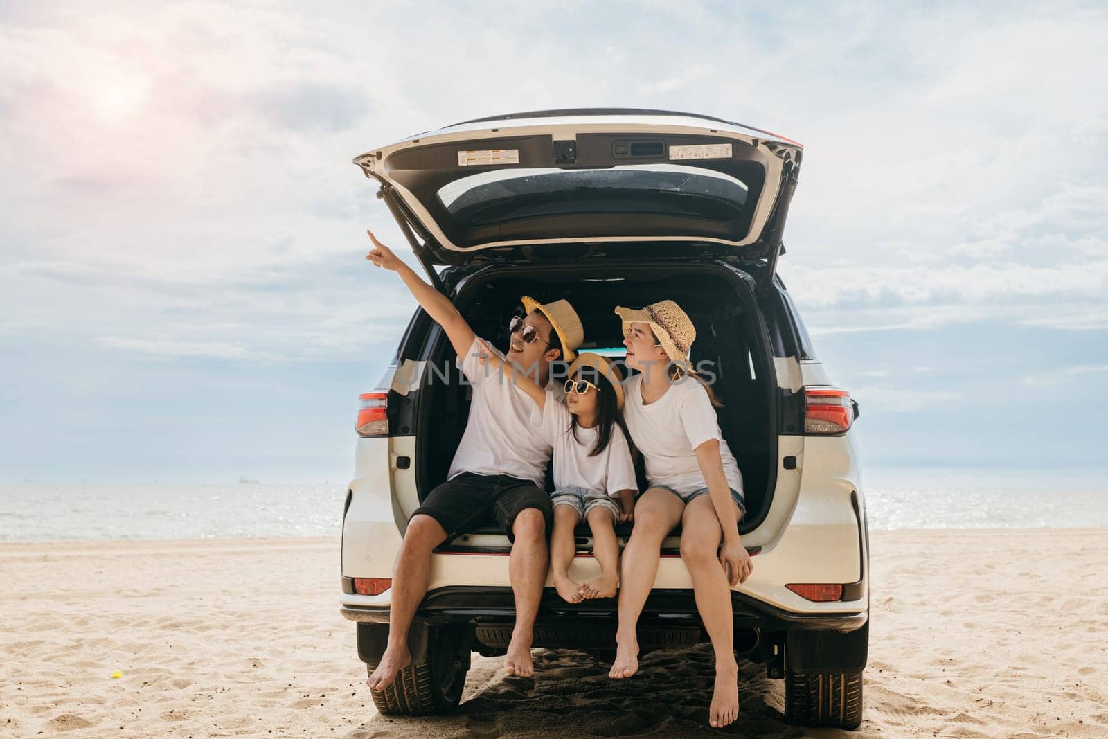 Happy Family Day. Family travel in holiday at sea beach, Dad, mom, daughter enjoy road trip sitting on back car and pointing finger out, people having fun in summer vacation on beach with automobile