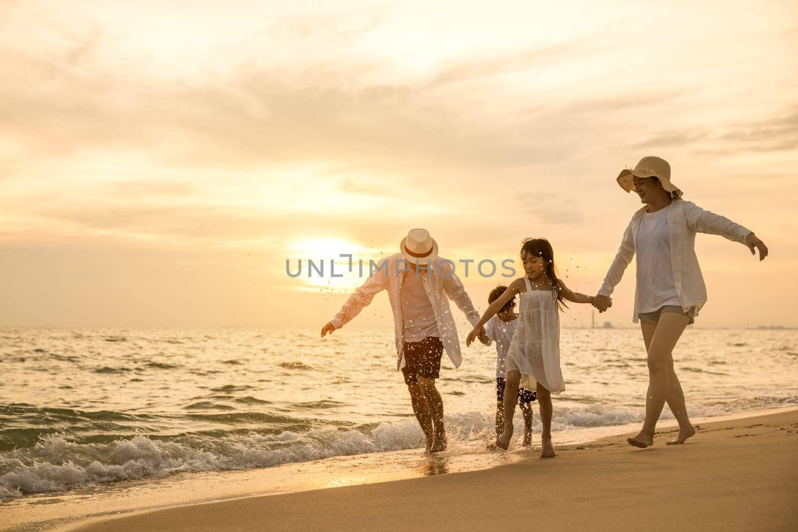 Happy family having fun running on a sandy beach at sunset time by Sorapop