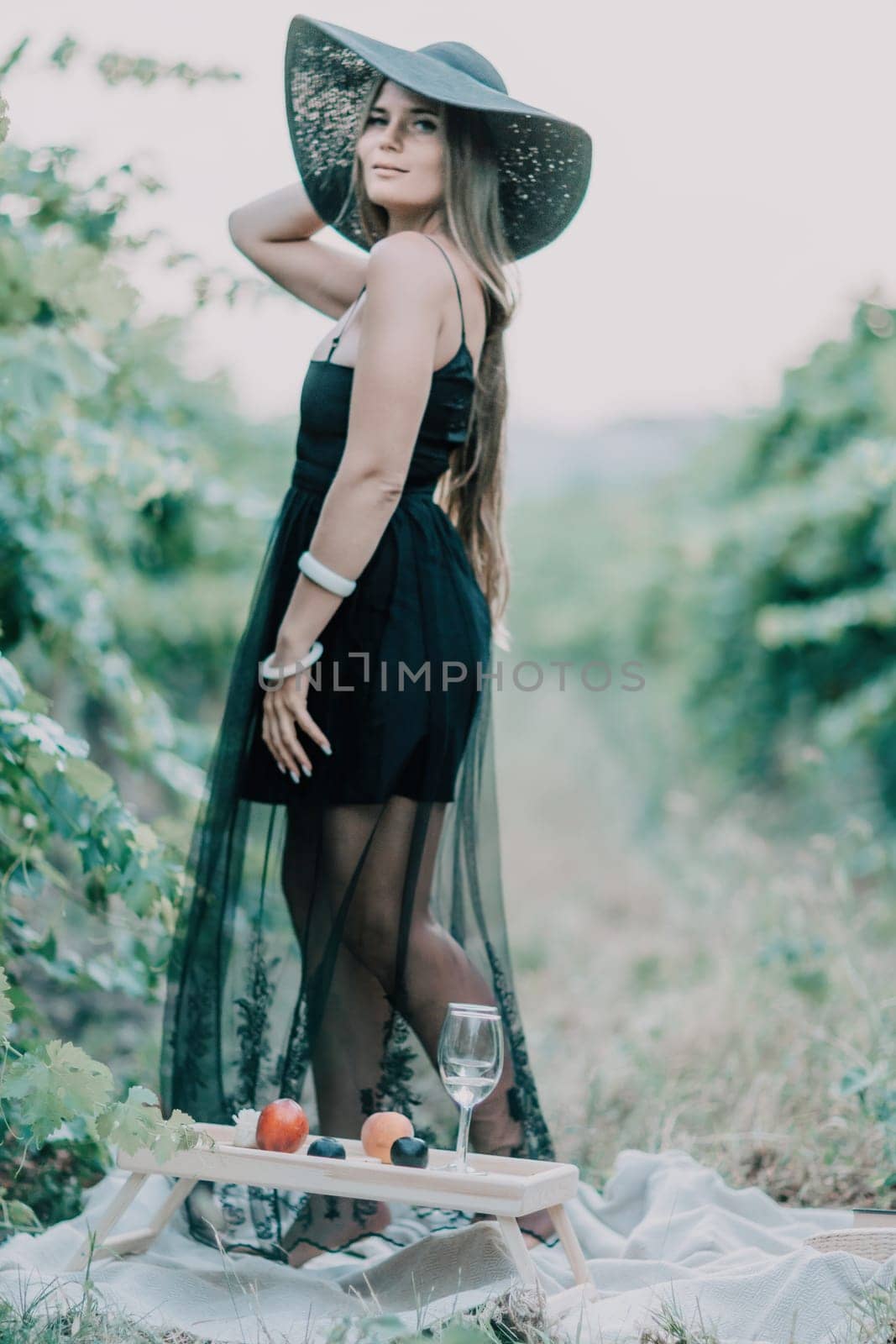Woman travel winery. Portrait of happy woman holding glass of wine and enjoying in vineyard. Elegant young lady in hat toasting with wineglass smiling cheerfully enjoying her stay at vineyard. by panophotograph