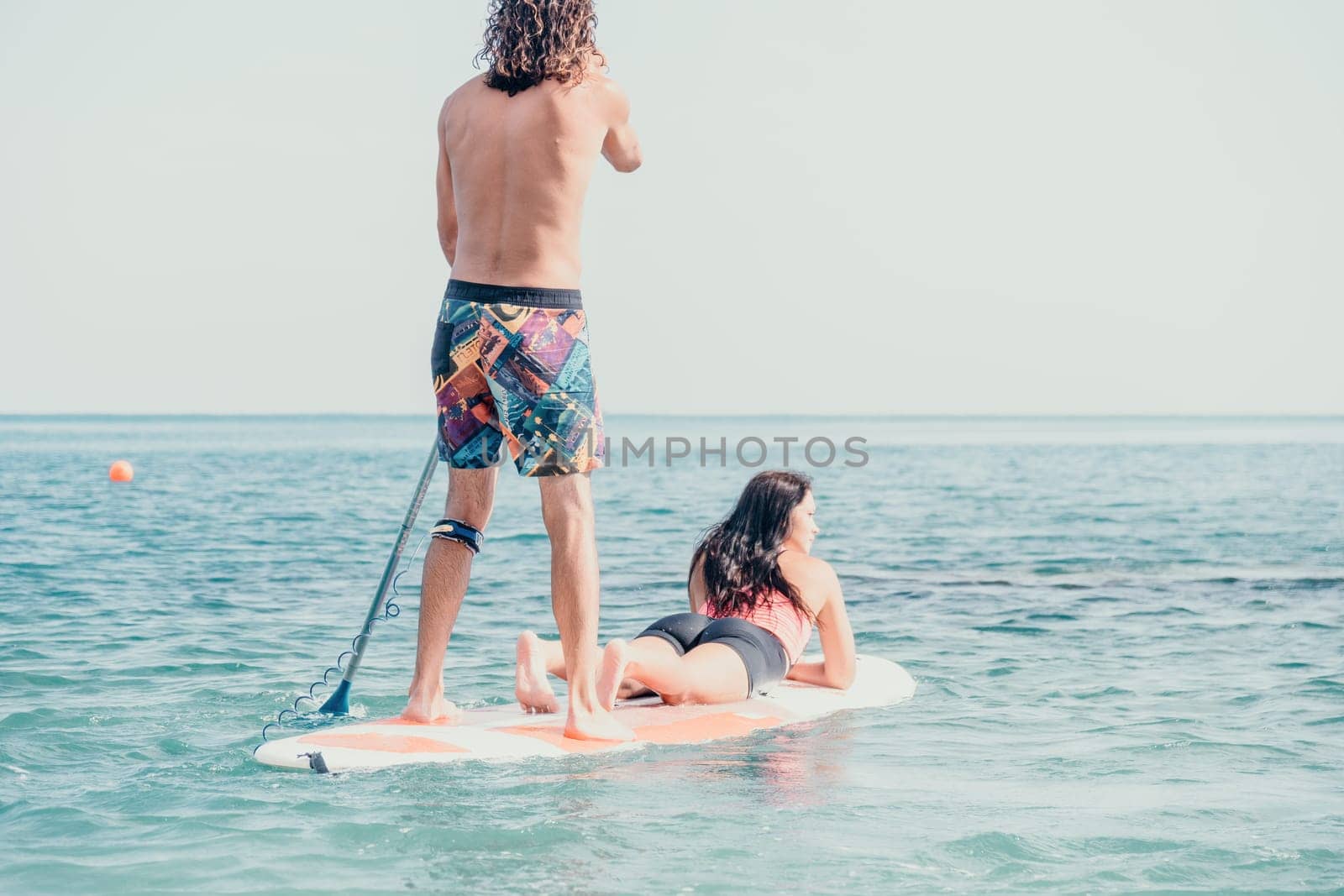 Sea woman and man on sup. Silhouette of happy young woman and man, surfing on SUP board, confident paddling through water surface. Idyllic sunset. Active lifestyle at sea or river. by panophotograph