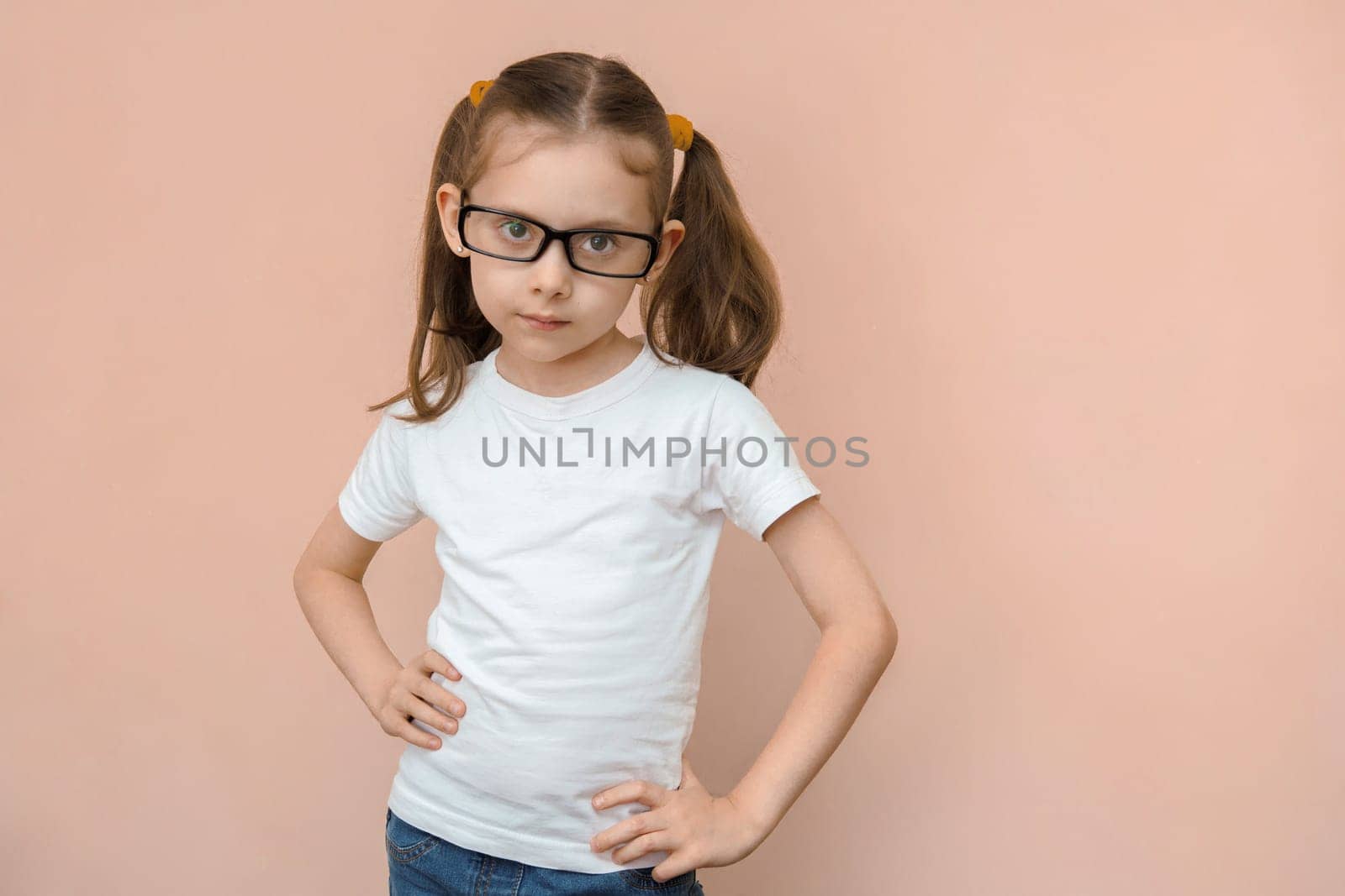 Caucasian cute girl 5 - 7 years old in a white T-shirt and jeans with diopter glasses, studio portrait.