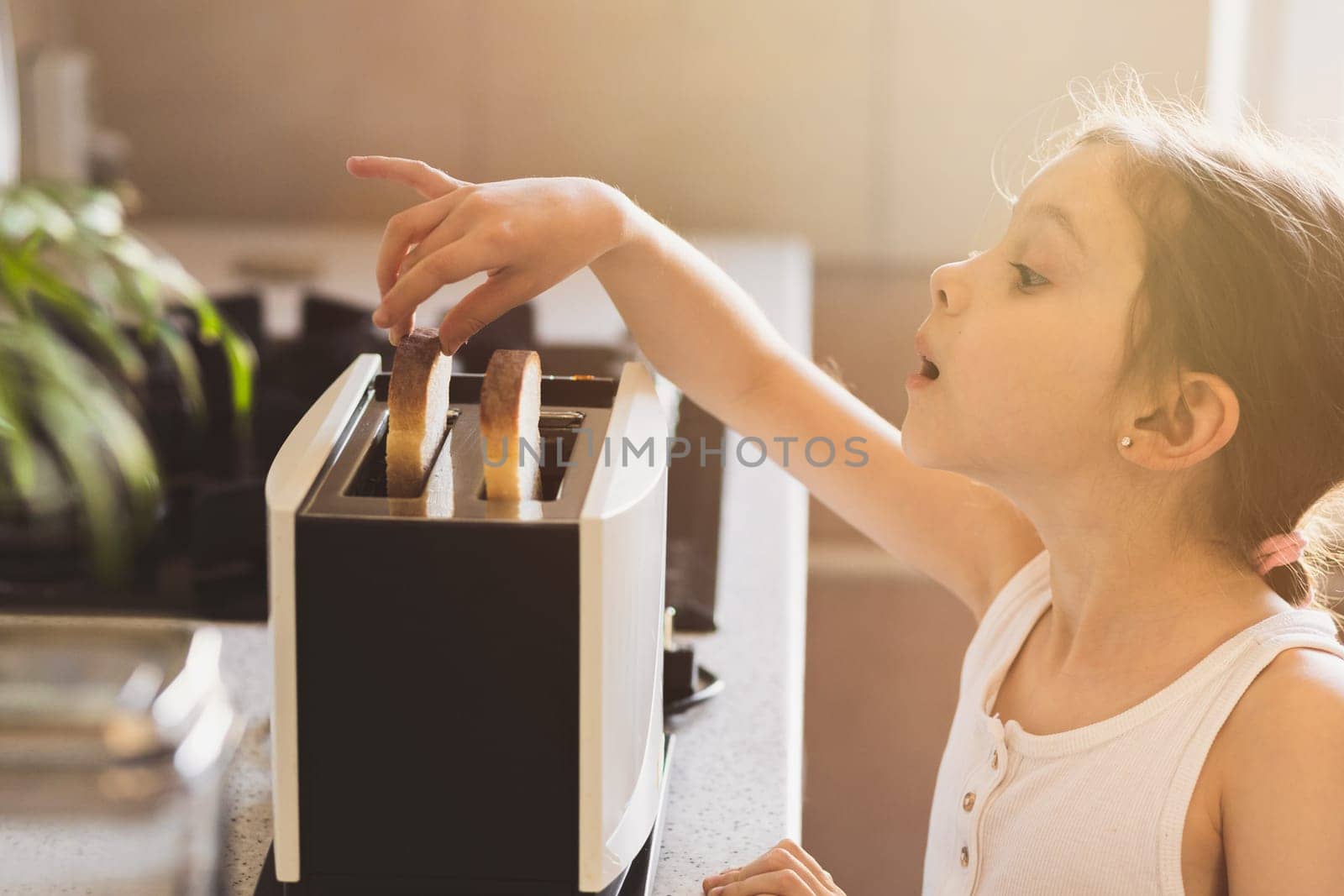 Funny caucasian emotional girl 7 years old preparing breakfast in the kitchen, selective soft focus, lifestyle home portrait.