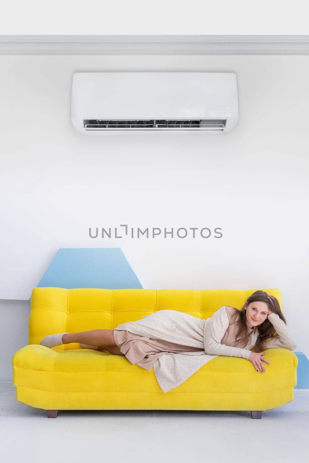 Young happy caucasian woman lies on a yellow sofa in bright interior with copy space, vertical.
