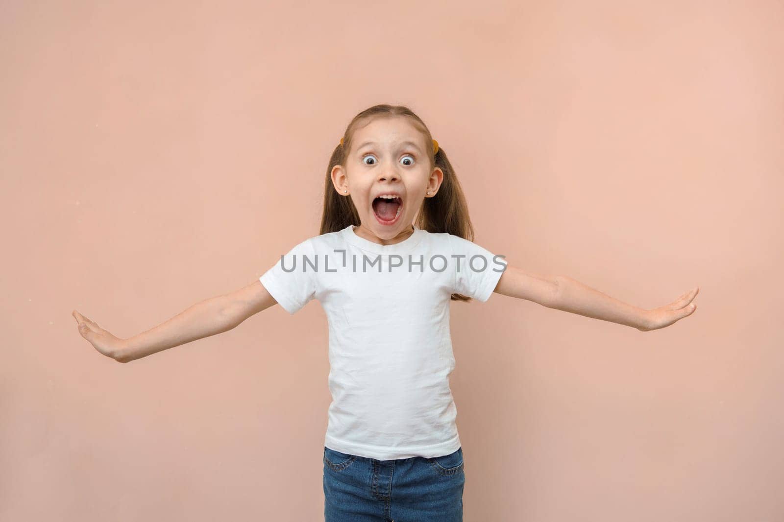 Shocked emotional caucasian girl 7 years old in a white t-shirt on a pink background.