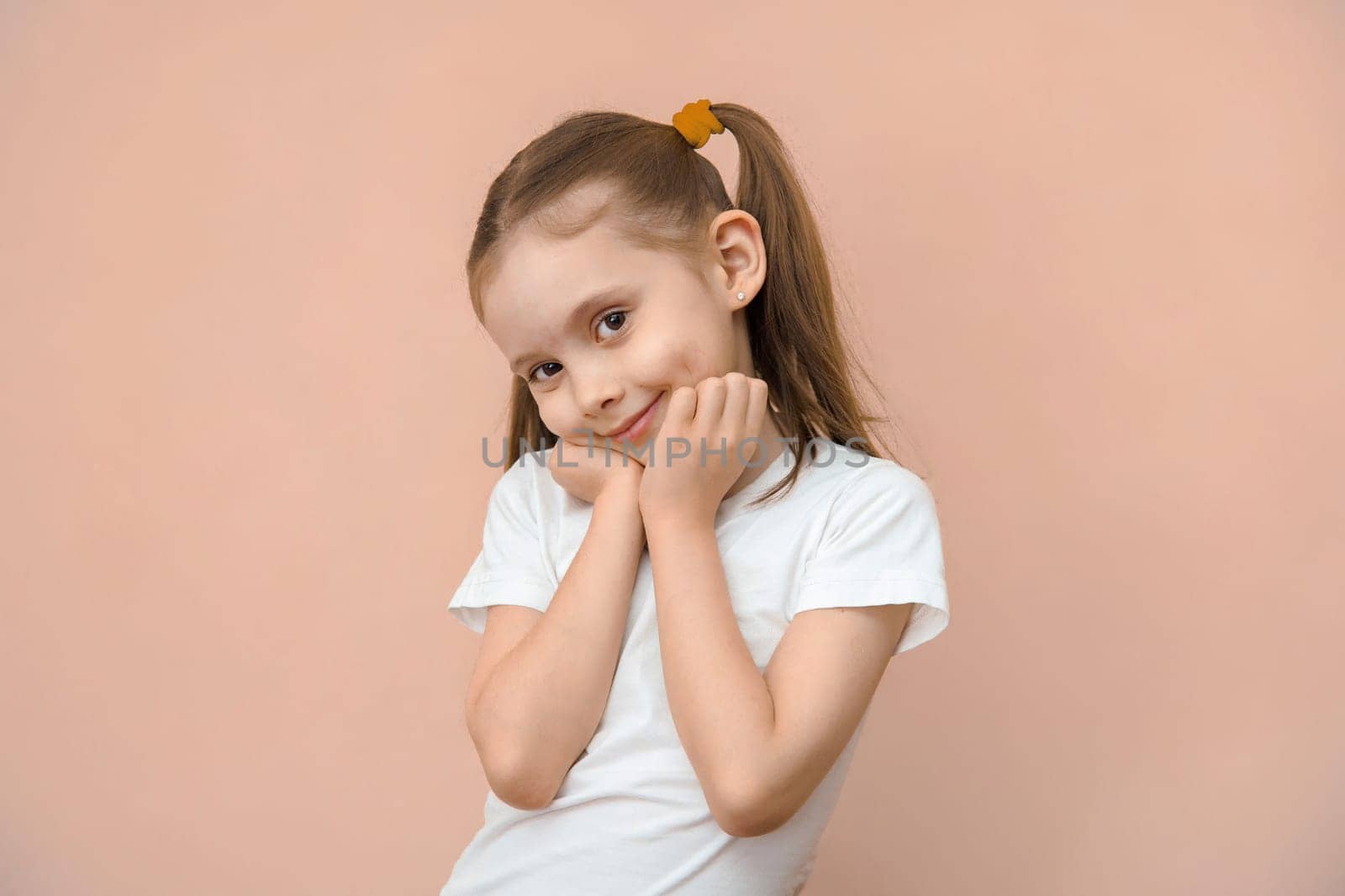 Cute caucasian preschool girl 5-7 y.o. in a white t-shirt look at camera.