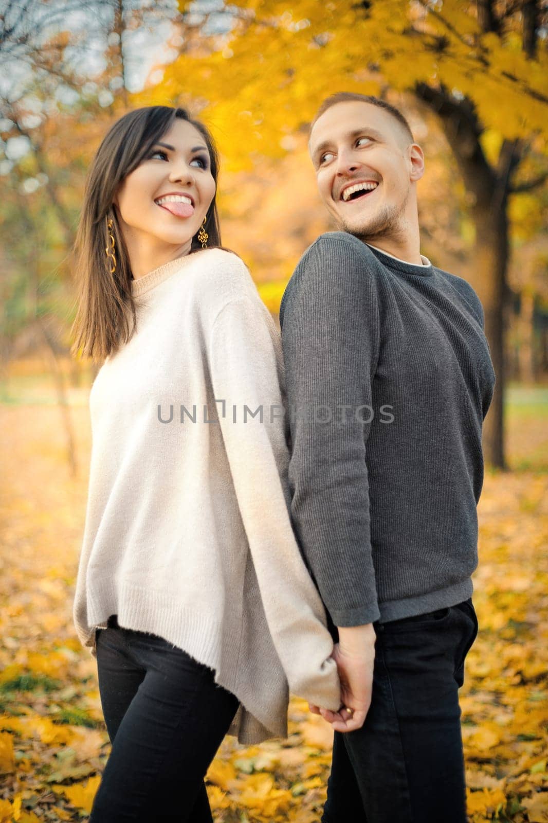 Young smiling couple looking at each other spending time together on weekends in autumn park.