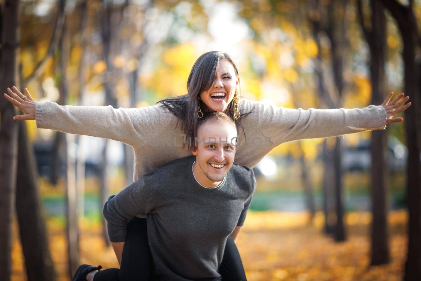 Happy caucasian man carrying his asian girlfriend on back in autumn outdoor.