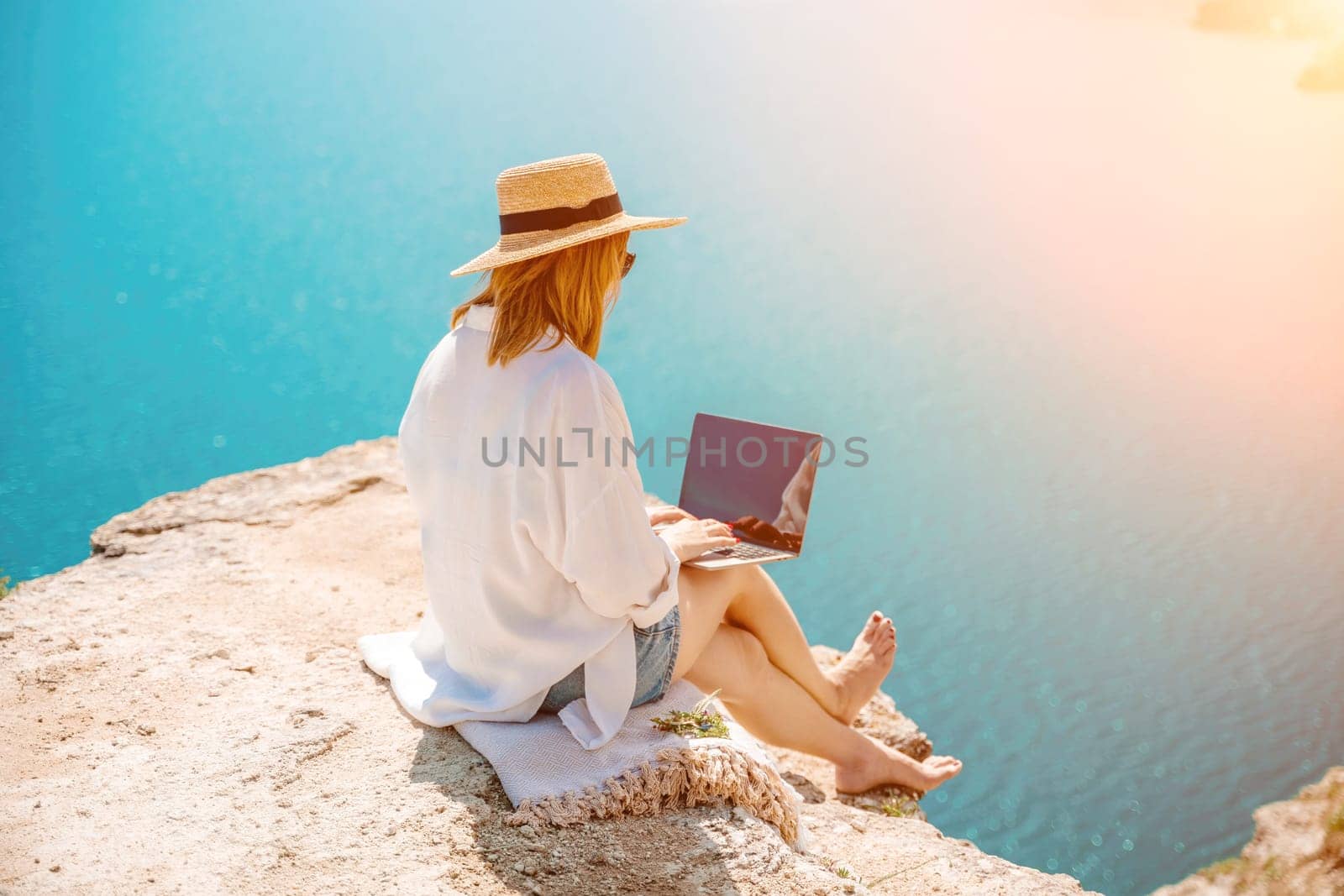 Freelance woman working on a laptop by the sea, typing away on the keyboard while enjoying the beautiful view, highlighting the idea of remote work