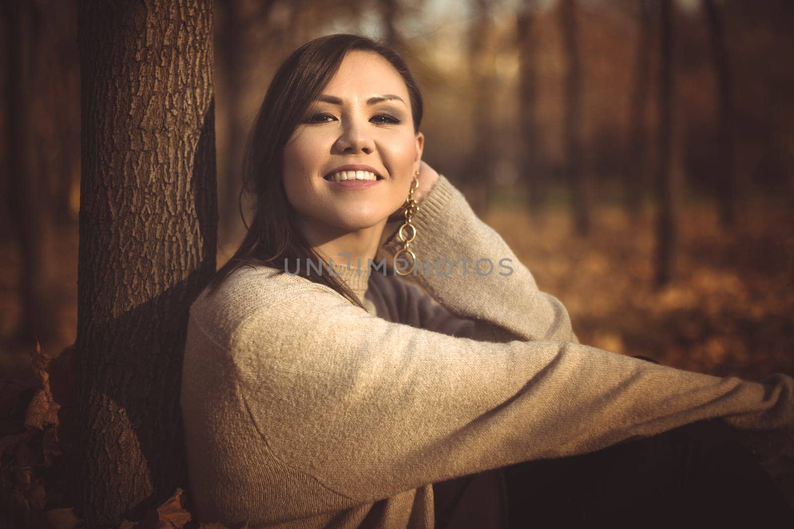 Young happy mixed race woman sitting on the grass in the park in autumn, toned photo.