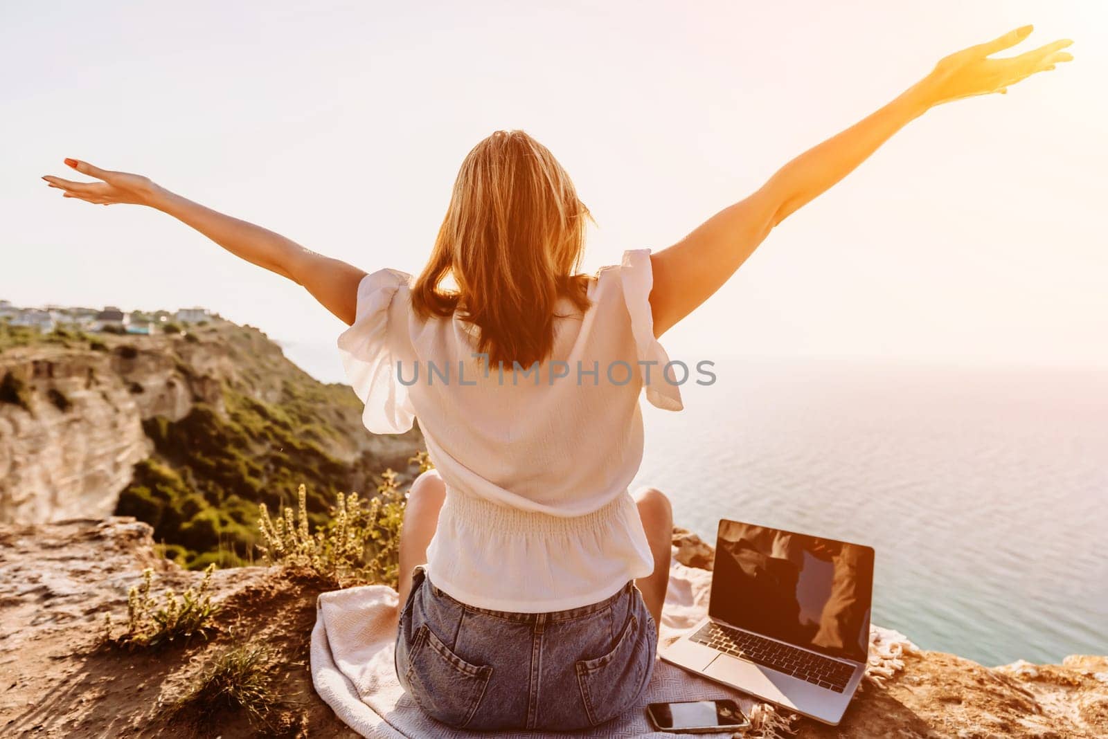 Freelance woman working on a laptop by the sea, typing away on the keyboard while enjoying the beautiful view, highlighting the idea of remote work