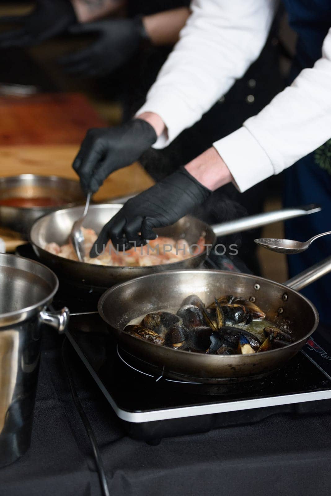 the chef in the restaurant is frying mussels in a steel pan.