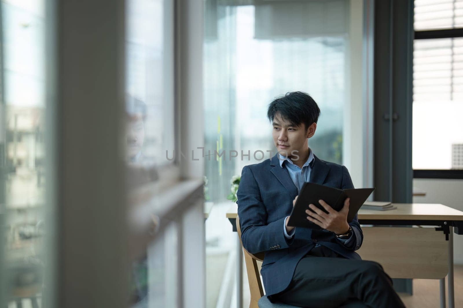 Young Asian businessman standing in an office smiling confidently..