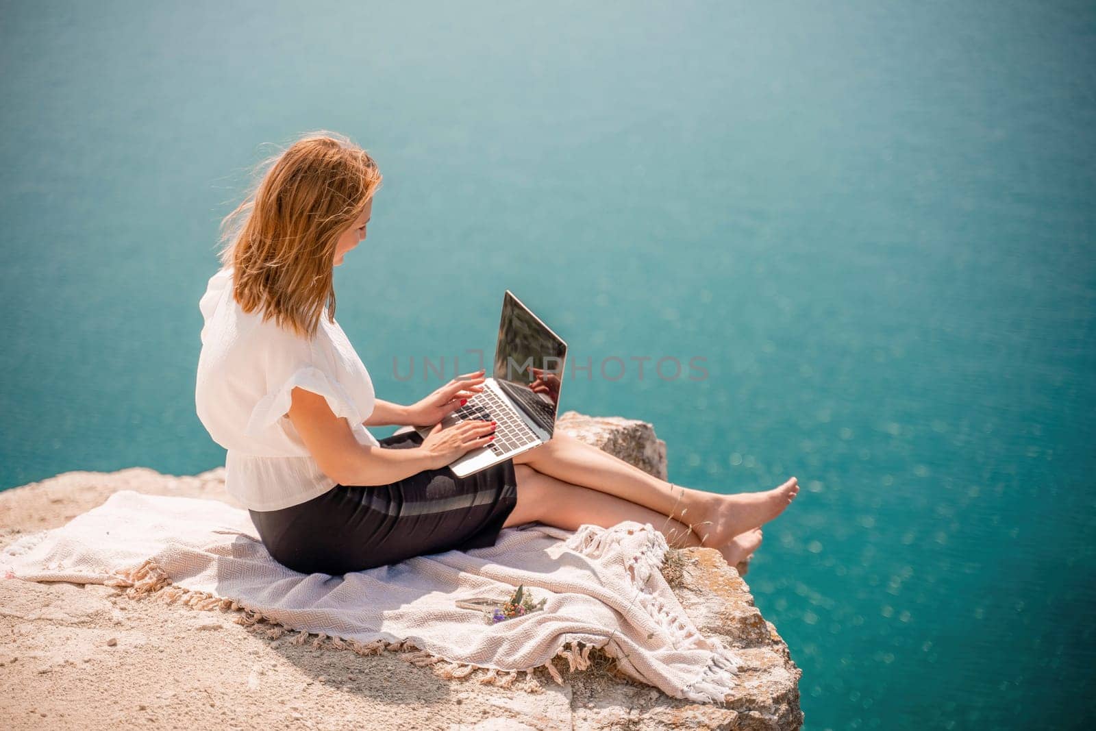 Freelance women sea working on the computer. Good looking middle aged woman typing on a laptop keyboard outdoors with a beautiful sea view. The concept of remote work