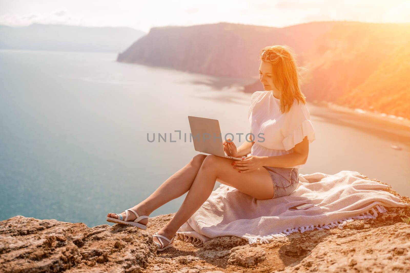 Freelance woman working on a laptop by the sea, typing away on the keyboard while enjoying the beautiful view, highlighting the idea of remote work