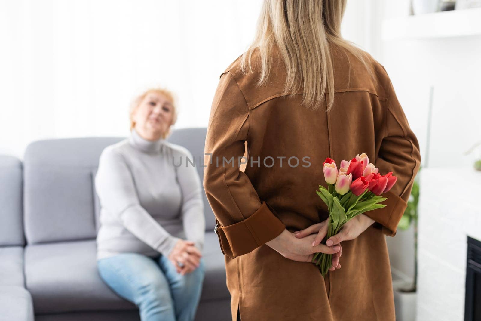 Beautiful young woman and her mother with flowers tulips in hands at home