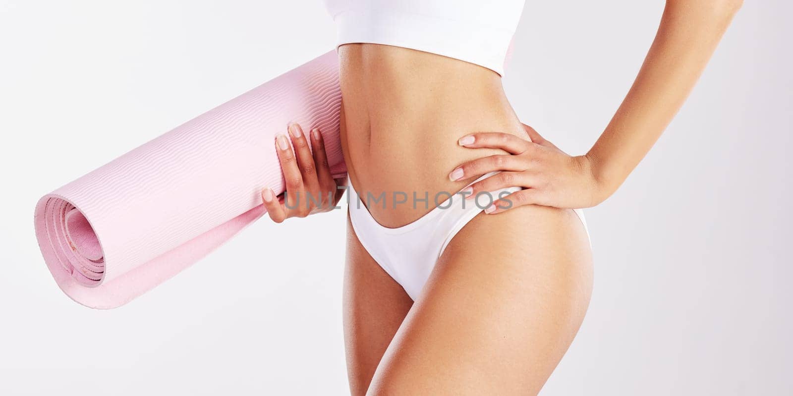 Get into shape with yoga. a fit young woman holding a yoga mat while standing against a studio background