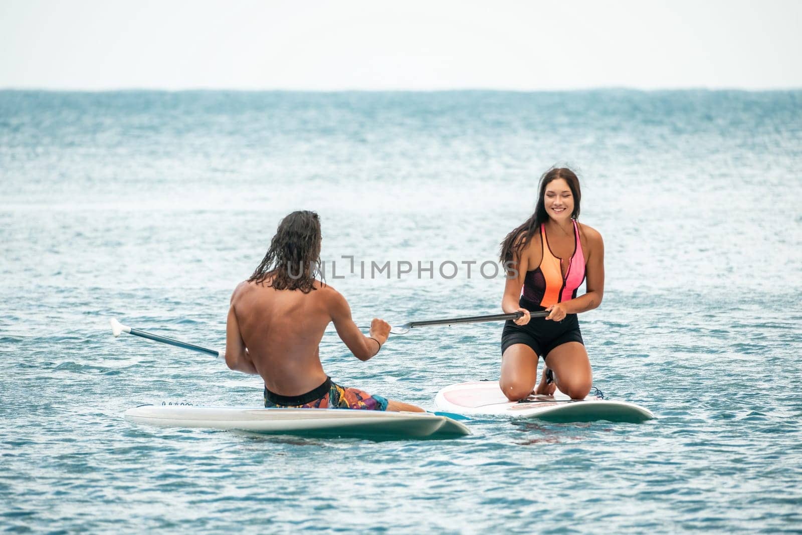 Sea woman and man on sup. Silhouette of happy young woman and man, surfing on SUP board, confident paddling through water surface. Idyllic sunset. Active lifestyle at sea or river