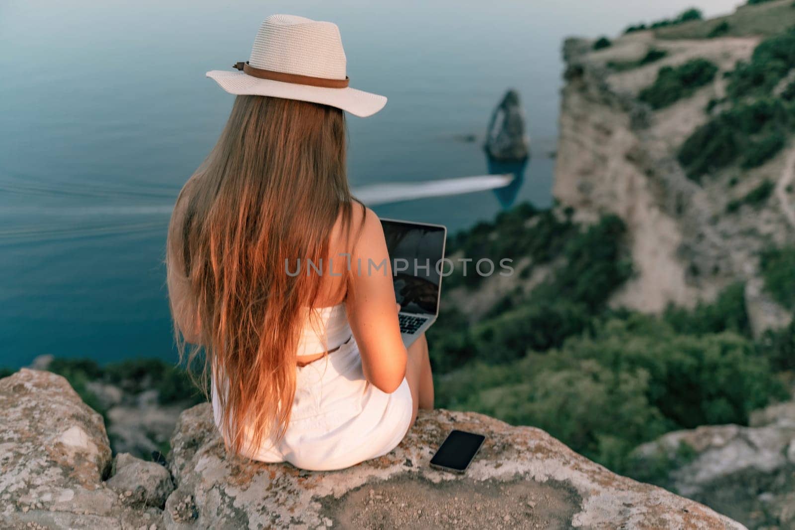 Freelance women sea working on the computer. Good looking middle aged woman typing on a laptop keyboard outdoors with a beautiful sea view. The concept of remote work