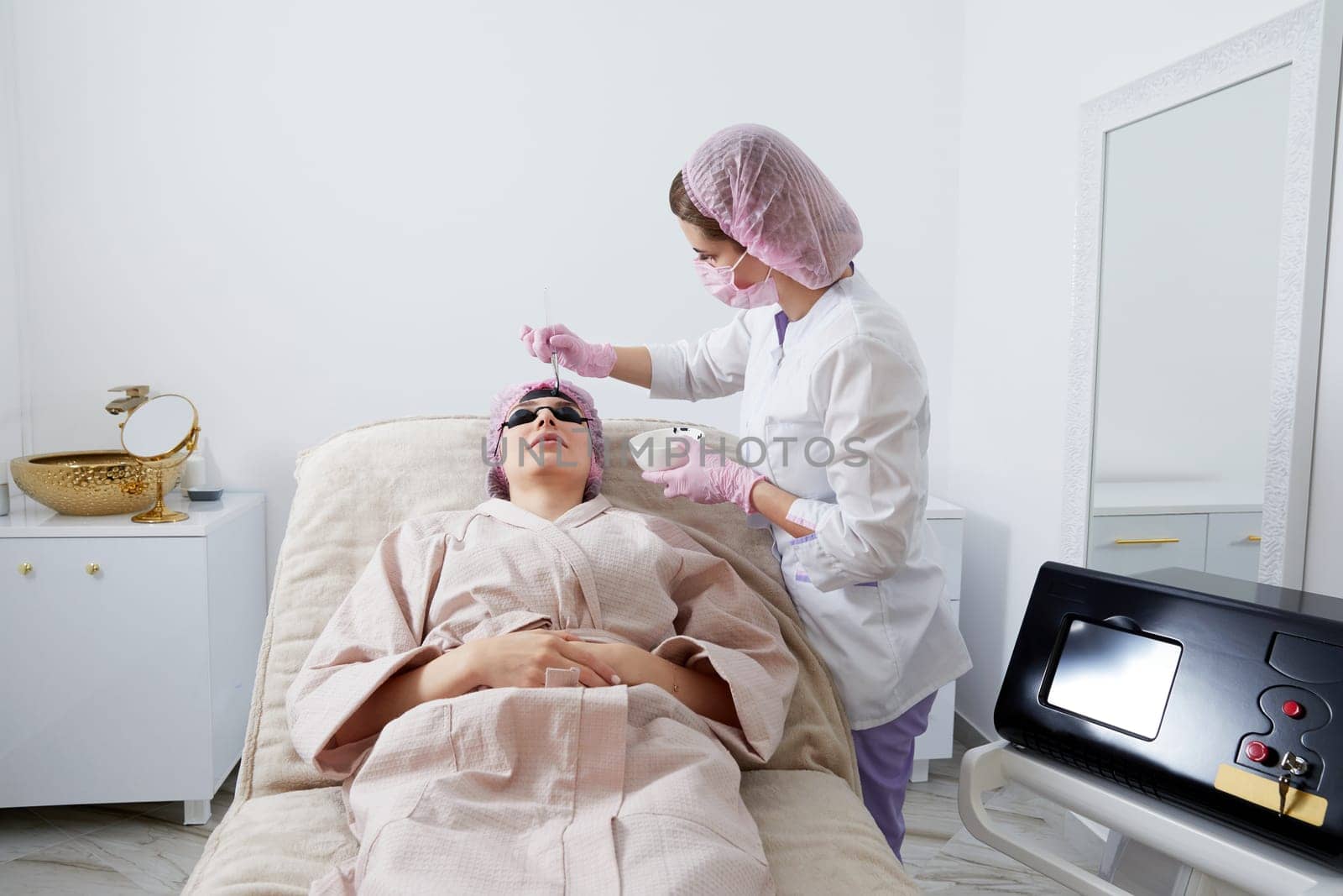 Carbon peeling in beauty salon. Cosmetologist applying black mask on the face of a beautiful woman for carbon peeling by Mariakray