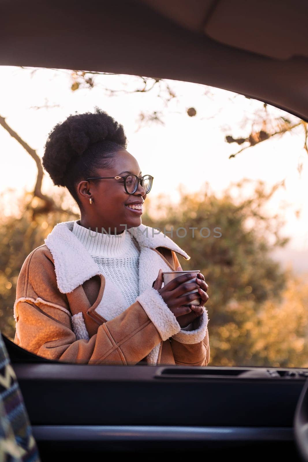 young african woman traveling in a camper van smiling happy in nature with a mug of hot drink in hand, concept of morning bliss and wilderness lifestyle