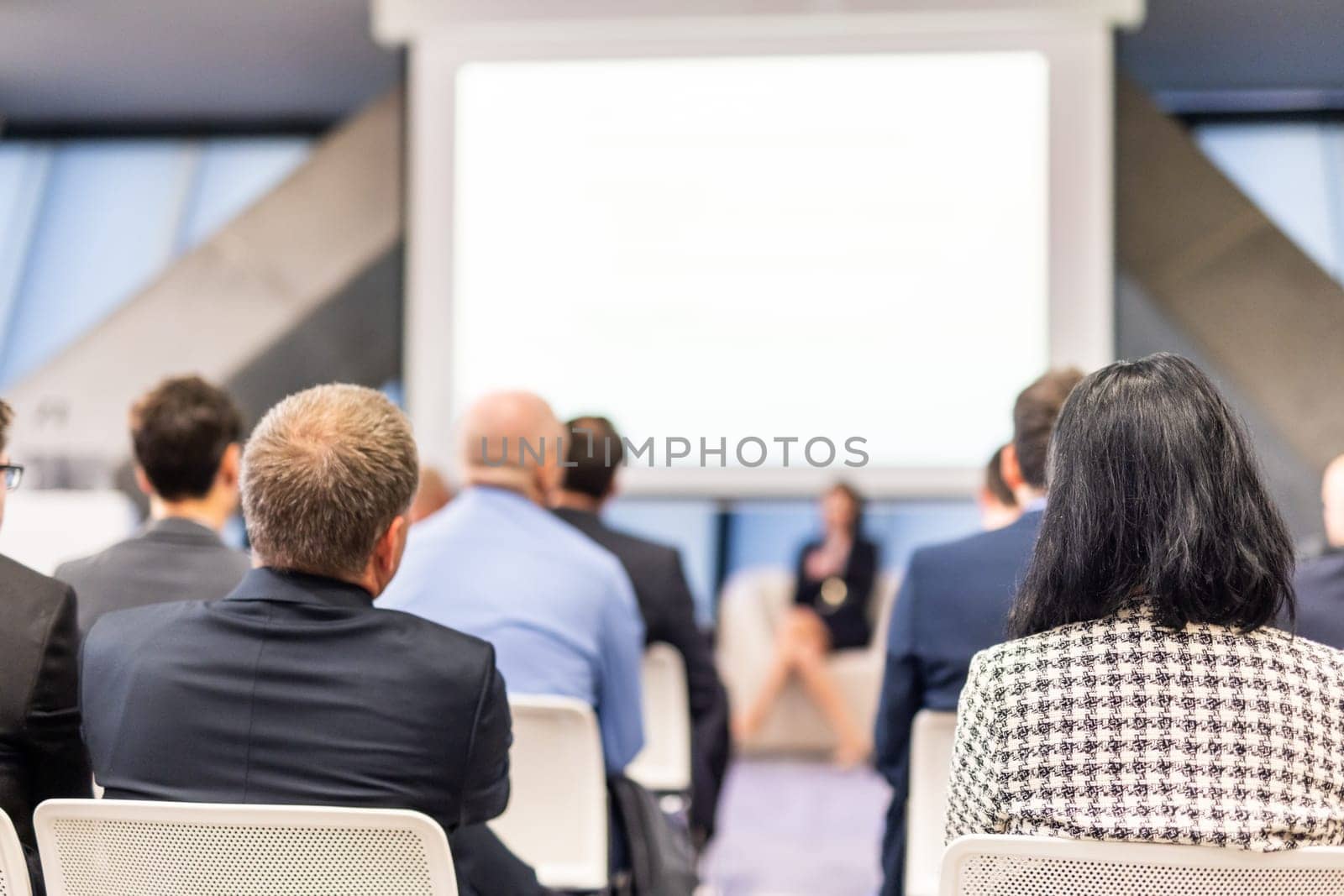 Business and entrepreneurship symposium. Female speaker giving a talk at business meeting. Audience in conference hall. Rear view of unrecognized participant in audience.