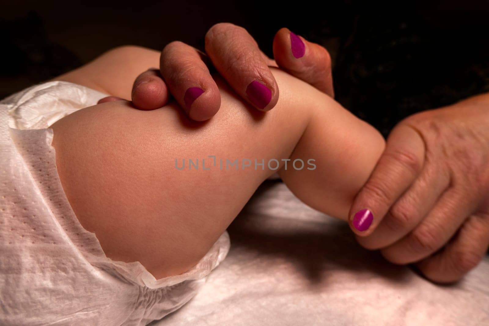 baby feet. massage. The hands of an adult - a mother or a masseur - massage a little girl. Dark background