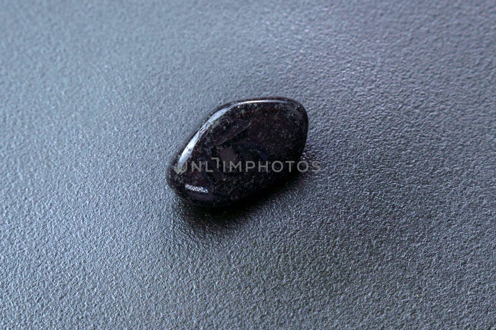 Close up of natural mineral from geological collection tumbled black onyx gem stone, black background by darksoul72