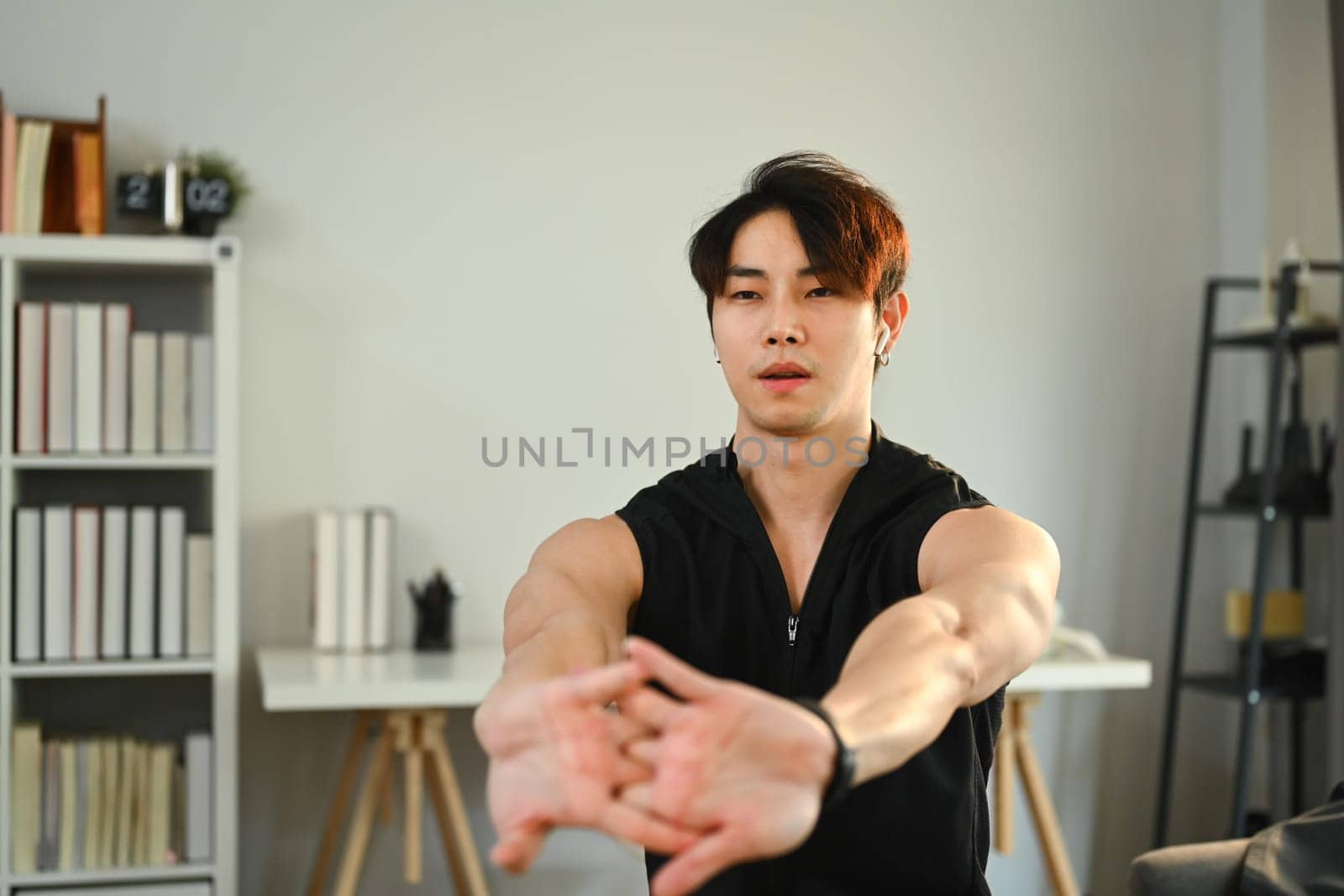 Athletic man in sportswear stretching arms before workout routine at home. Fitness, training and healthy lifestyle concept by prathanchorruangsak